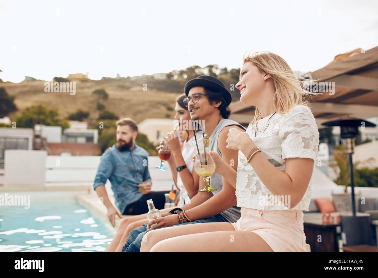 Felice giovani amici seduti a bordo piscina con un cocktail. Giovani relax presso la piscina con i piedi in acqua dur Foto Stock