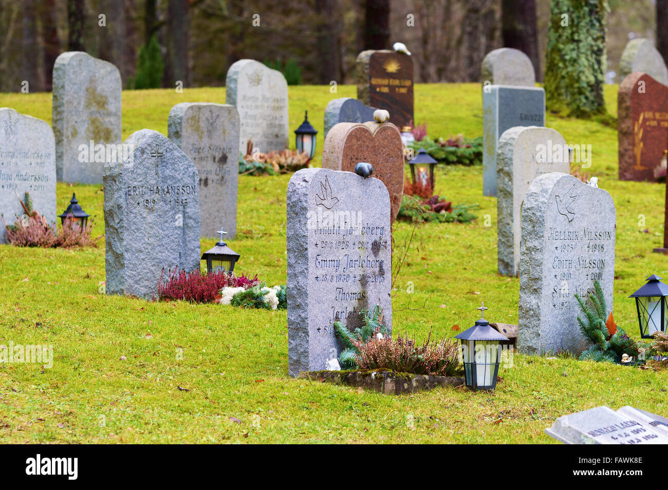 Ronneby, Svezia - 23 dicembre 2015: GRANITO lapidi al cimitero Bredakra. Lanterne sono posti da alcune pietre. Forest visibile Foto Stock