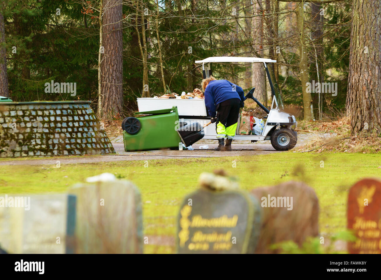 Ronneby, Svezia - 29 dicembre 2015: Sconosciuto cimitero femmina lavoratore una Vuota cestino in plastica con una pala in un piccolo veicolo Foto Stock