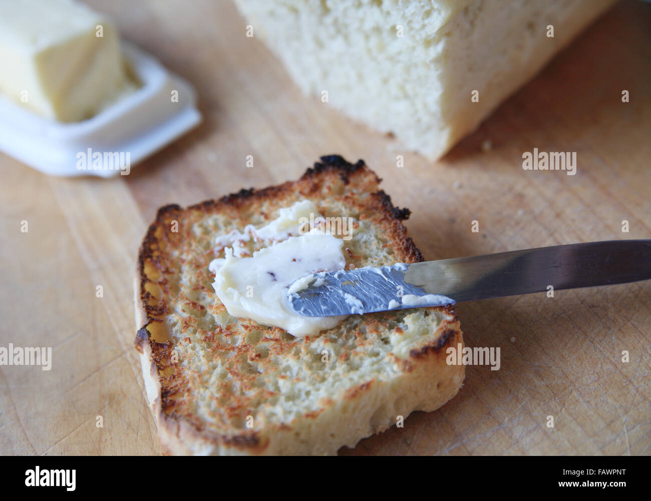 Diffusione di burro su una fetta di pane tostato con un piatto di burro e pane fatti in casa del pane dietro Foto Stock
