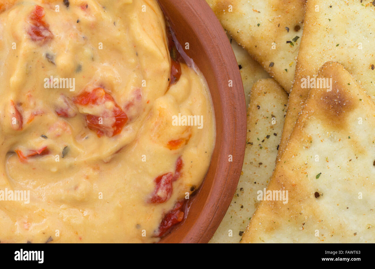 Top vista ravvicinata di una piccola ciotola con un serving di hummus con peperoni rossi plus pita snack crackers. Foto Stock