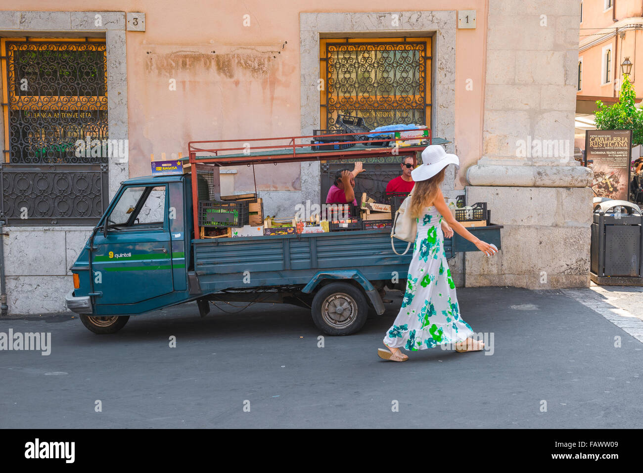 Uomo cerca Donna, vista di due uomini guardando una giovane donna in una  lunga estate vestito come lei cammina in passato a fornitori di frutta "  carrello a Taormina, in Sicilia Foto