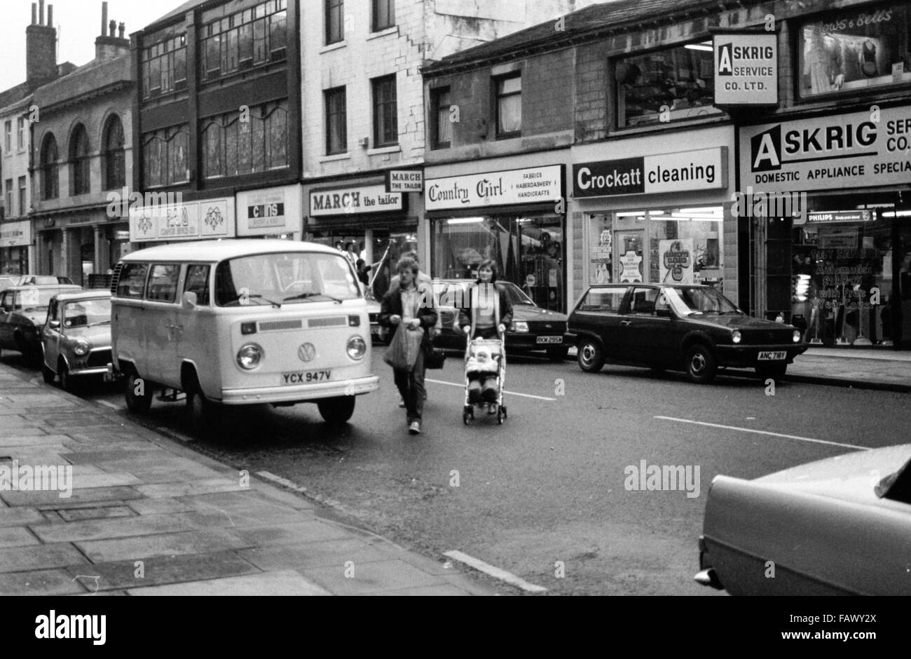 North Parade, Bradford, West Yorkshire, Regno Unito. Negozi locali e due donne con sedia push, passeggino attraversamento strada 1982. Foto Stock