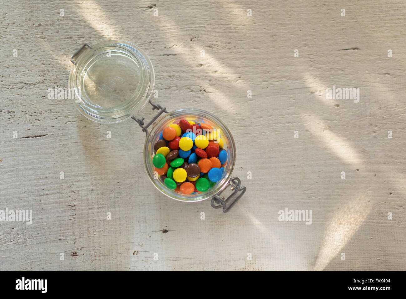 Rivestite e colorate di cioccolatini in un barattolo di vetro su legno tavolo bianco con macchie solari sul tavolo. Foto Stock