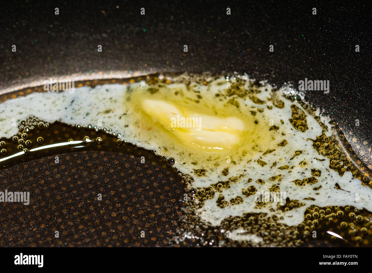 Macro Close-up di un pezzo di burro lentamente la fusione e la formazione di bolle in Teflon nero padella. Foto Stock