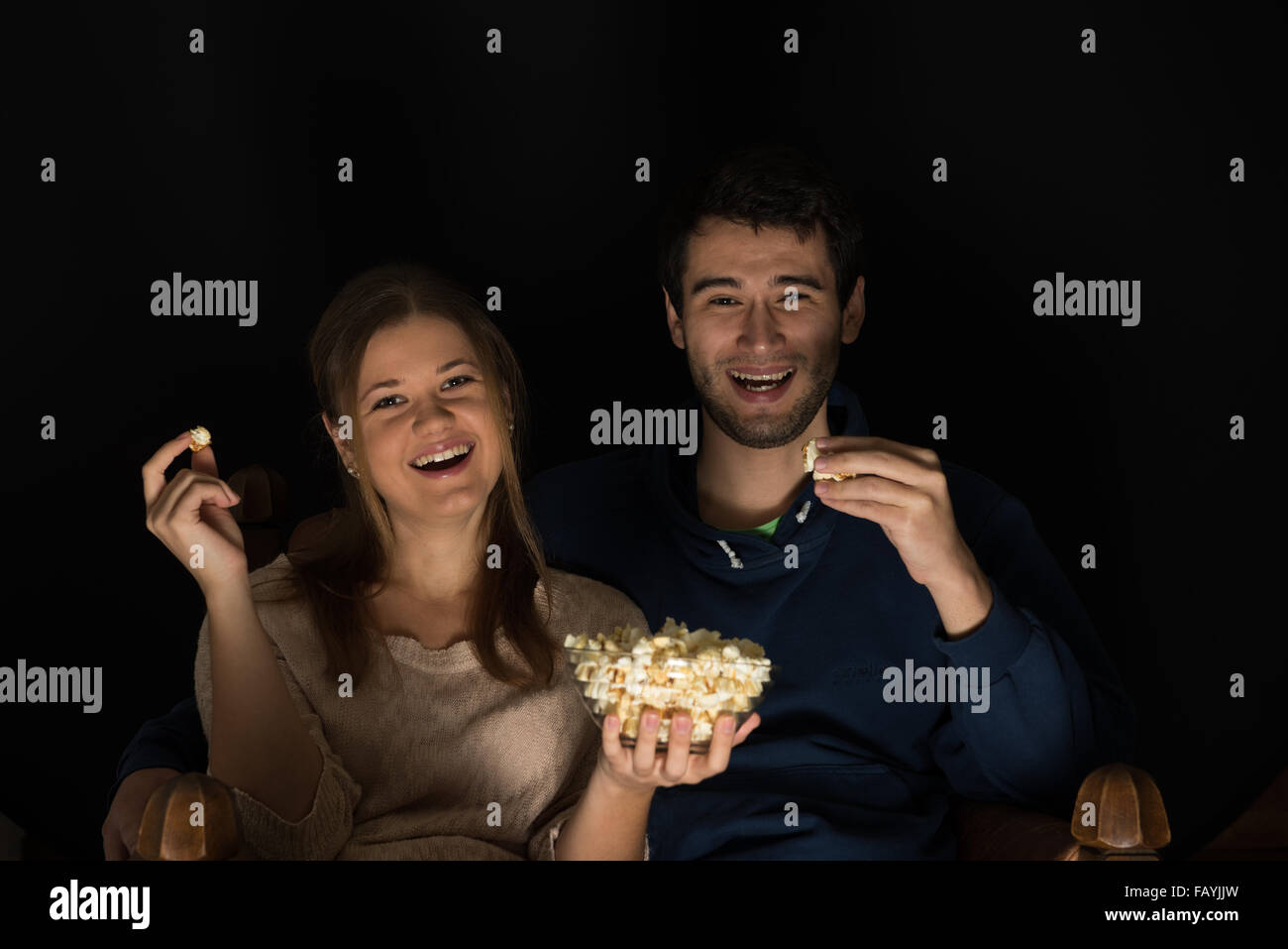 Coppia giovane, uomo e donna, seduti nella sala buia nella parte anteriore della tv guardare film e mangiare popcorn, mostrare le emozioni Foto Stock