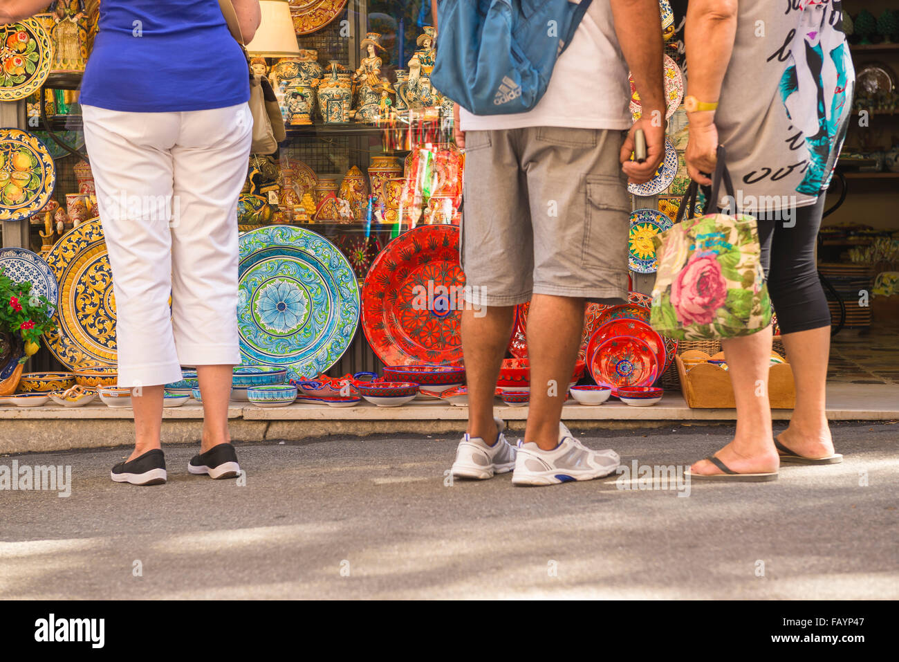 I turisti in Sicilia shopping, vista posteriore dei turisti in Taormina street pausa a guardare colorato di piastre in ceramica al di fuori di un negozio di souvenir, Sicilia. Foto Stock