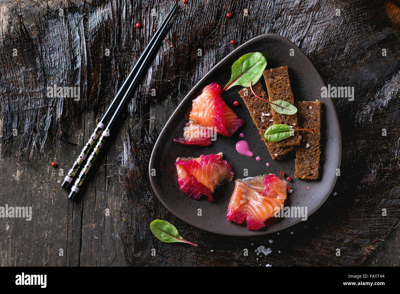 Triangolare piastra in ceramica con fette di filetto di salmone, salate con succo di barbabietola, servita con frumento integrale toast, foglie di insalata e Foto Stock