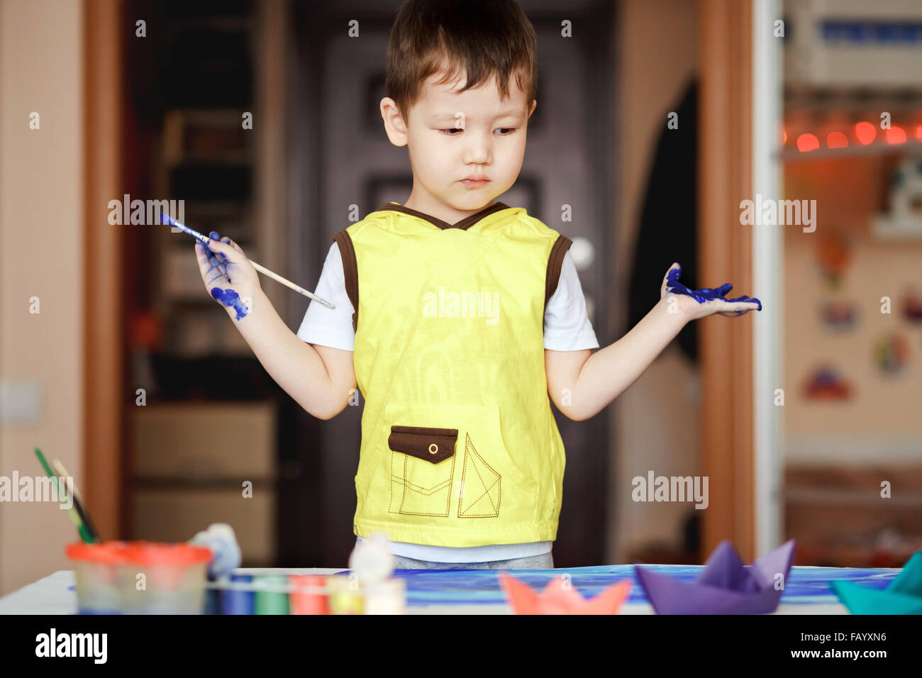 Little Boy in un giallo T-shirt colorate con della vernice dopo la pittura non sa cosa fare. Foto Stock