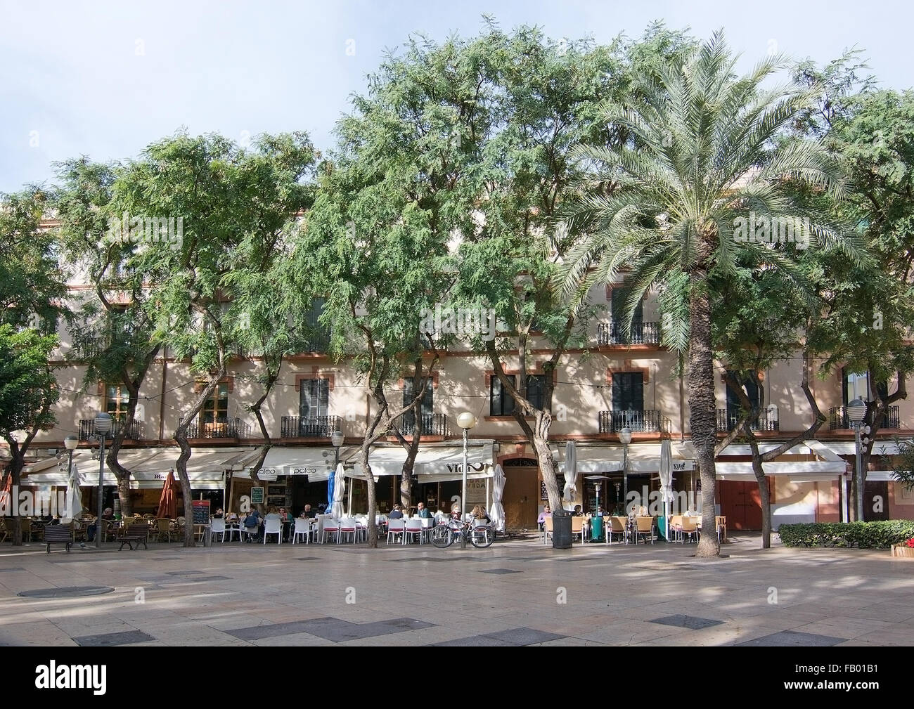 Ristoranti esterni e la vita urbana in una piazza con fresco verde di alberi nella città di Ibiza Foto Stock