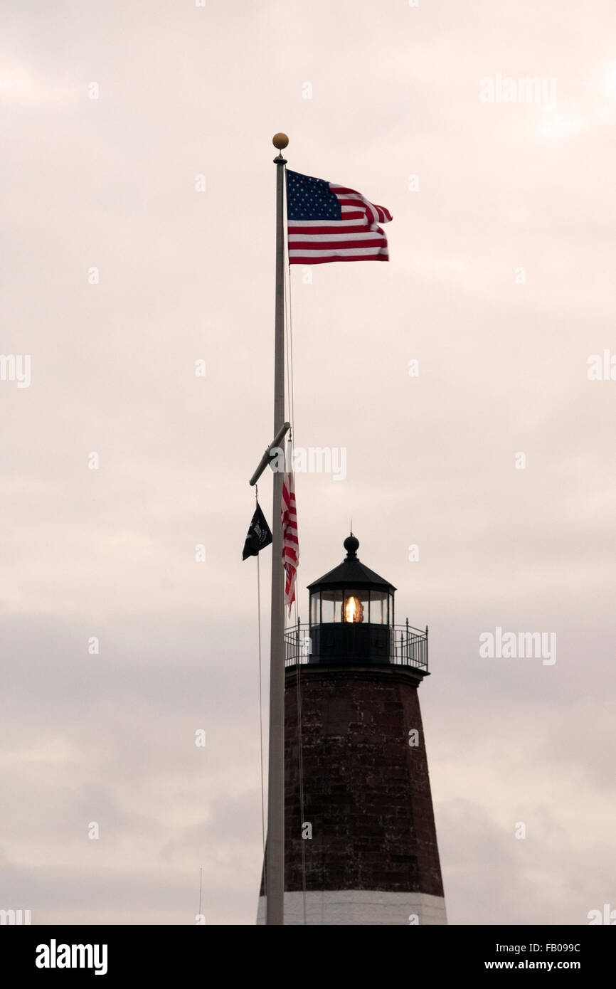 Bandiera americana onde di oltre il punto Judith torre faro come il faro lampeggia la luce in Rhode Island al tramonto. Foto Stock