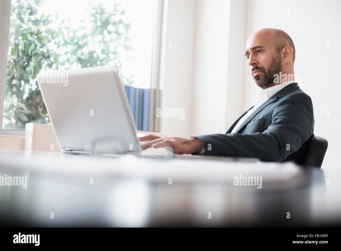 Imprenditore concentrato a lavorare con il computer portatile alla scrivania in ufficio Foto Stock