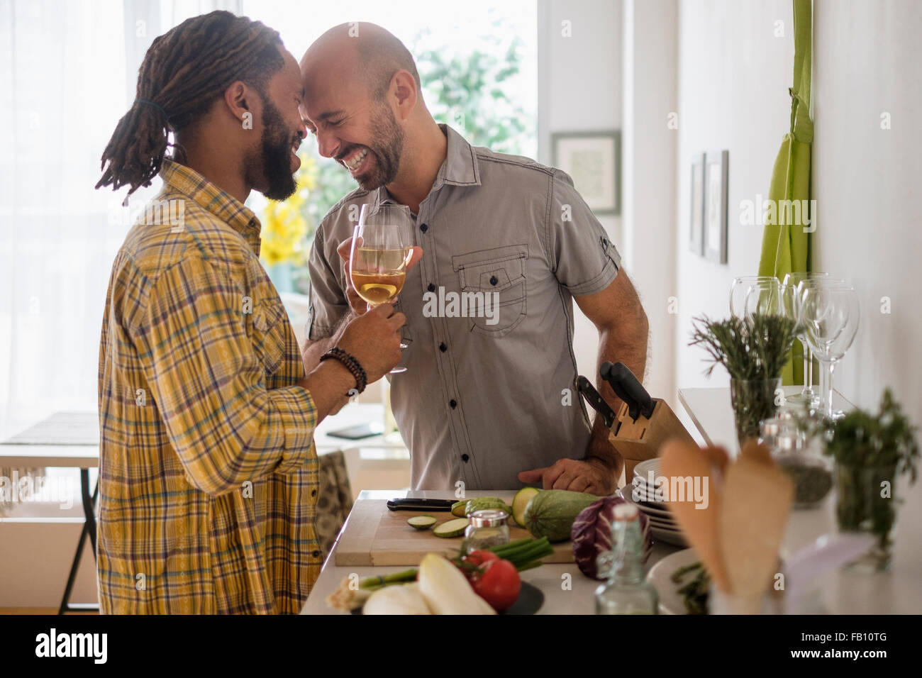 Smiley coppia omosessuale di bere vino in cucina Foto Stock