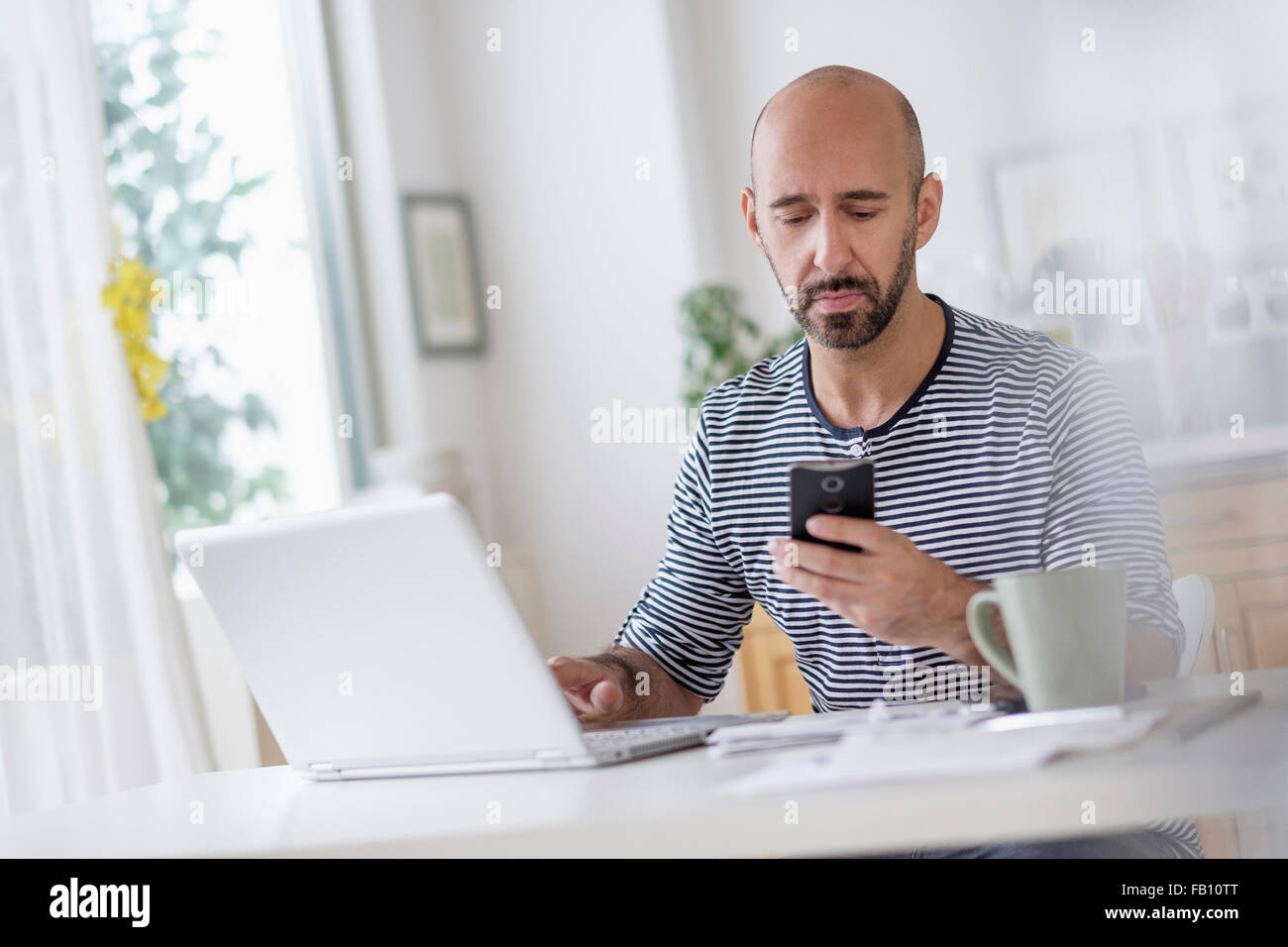 Uomo al lavoro con il computer portatile e tenendo premuto smart phone a tavola Foto Stock