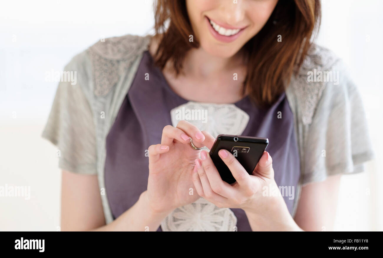 Donna sorridente la messaggistica di testo mediante lo smartphone Foto Stock