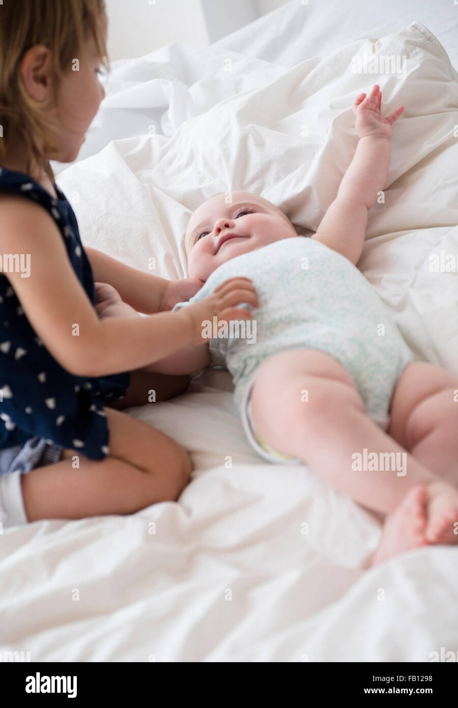 Baby girl (12-17 mesi) con la sorella (2-3) sul letto Foto Stock