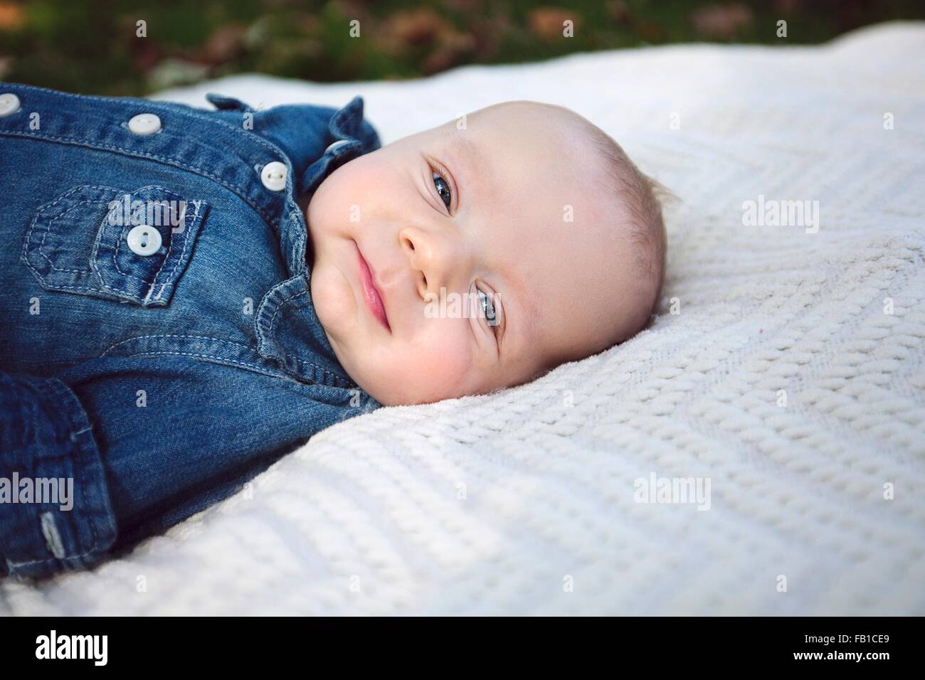 Vista laterale del baby boy indossando il denim shirt giacente sulla coperta guardando sorridente della fotocamera Foto Stock