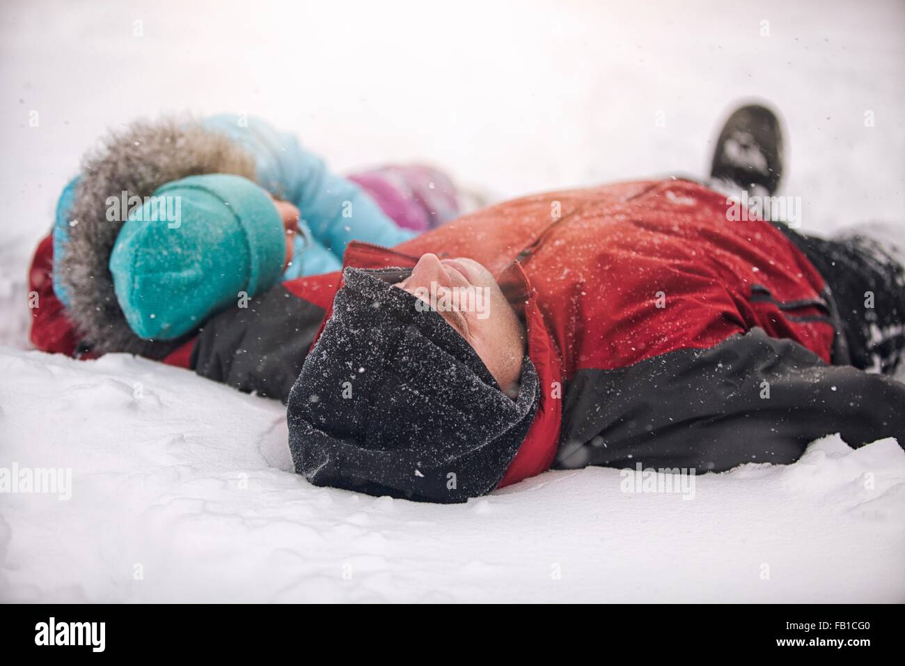Padre e figlia indossando cappelli di maglia giacente sul dorso nella neve Foto Stock
