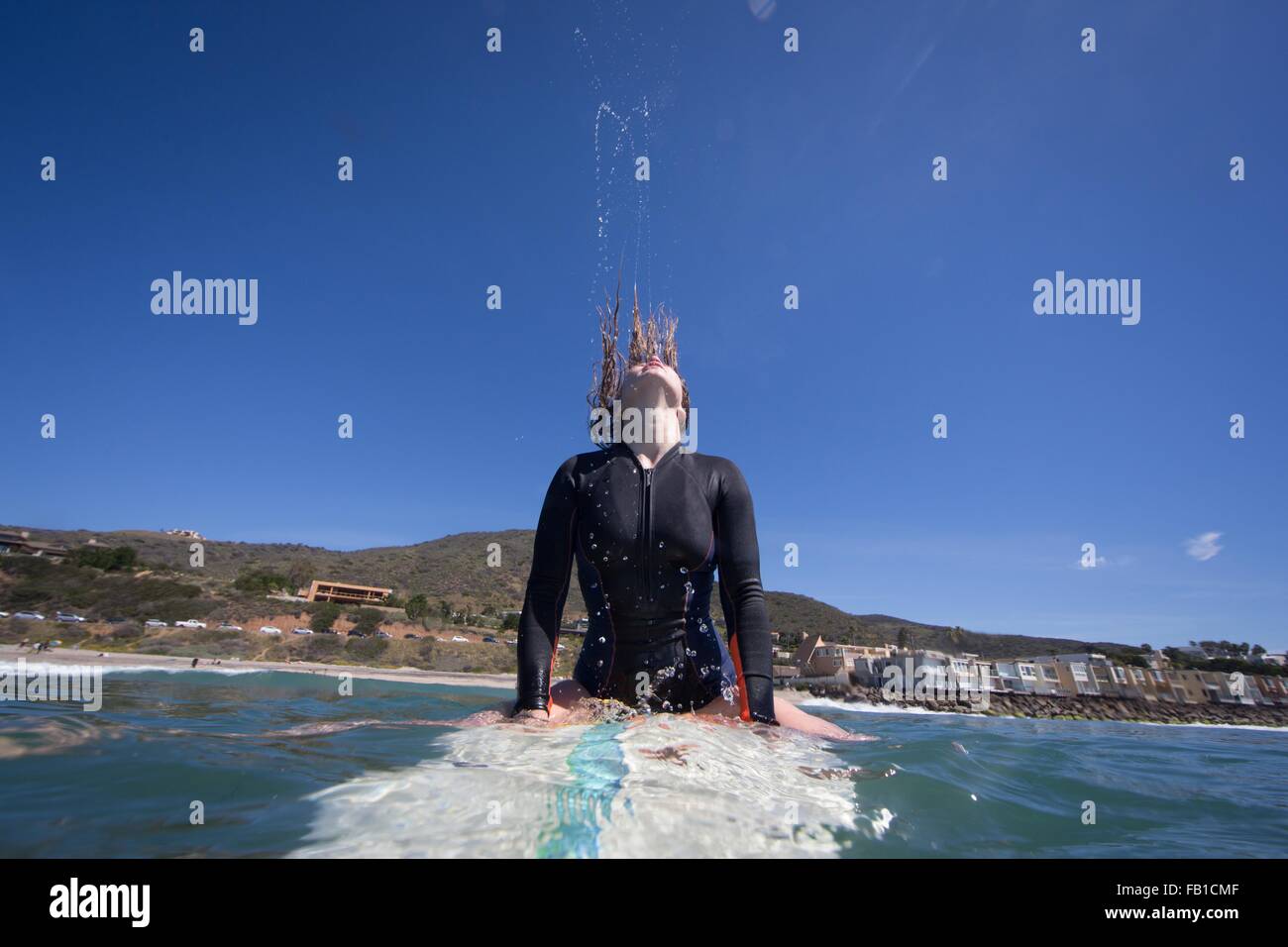 Vista frontale della giovane donna sulla tavola da surf gettando indietro i capelli umidi, Ventura, CALIFORNIA, STATI UNITI D'AMERICA Foto Stock