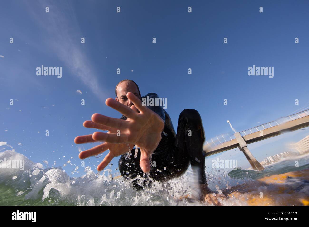 Basso angolo di visualizzazione di metà uomo adulto surf, guardando la telecamera, mostrando il palmo della mano, Los Angeles, California, Stati Uniti d'America Foto Stock