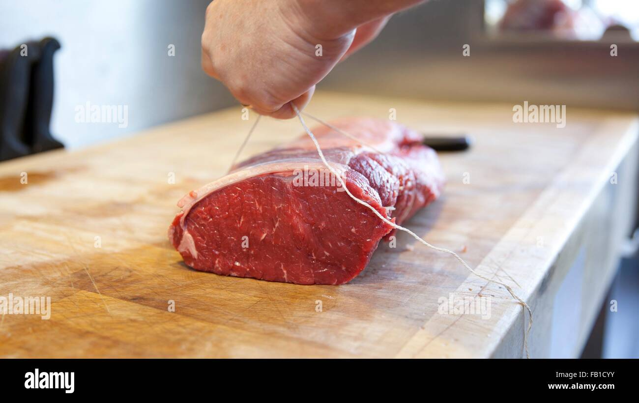 Close up dei macellai mani di carne di legatura giunto nel negozio di macellaio Foto Stock