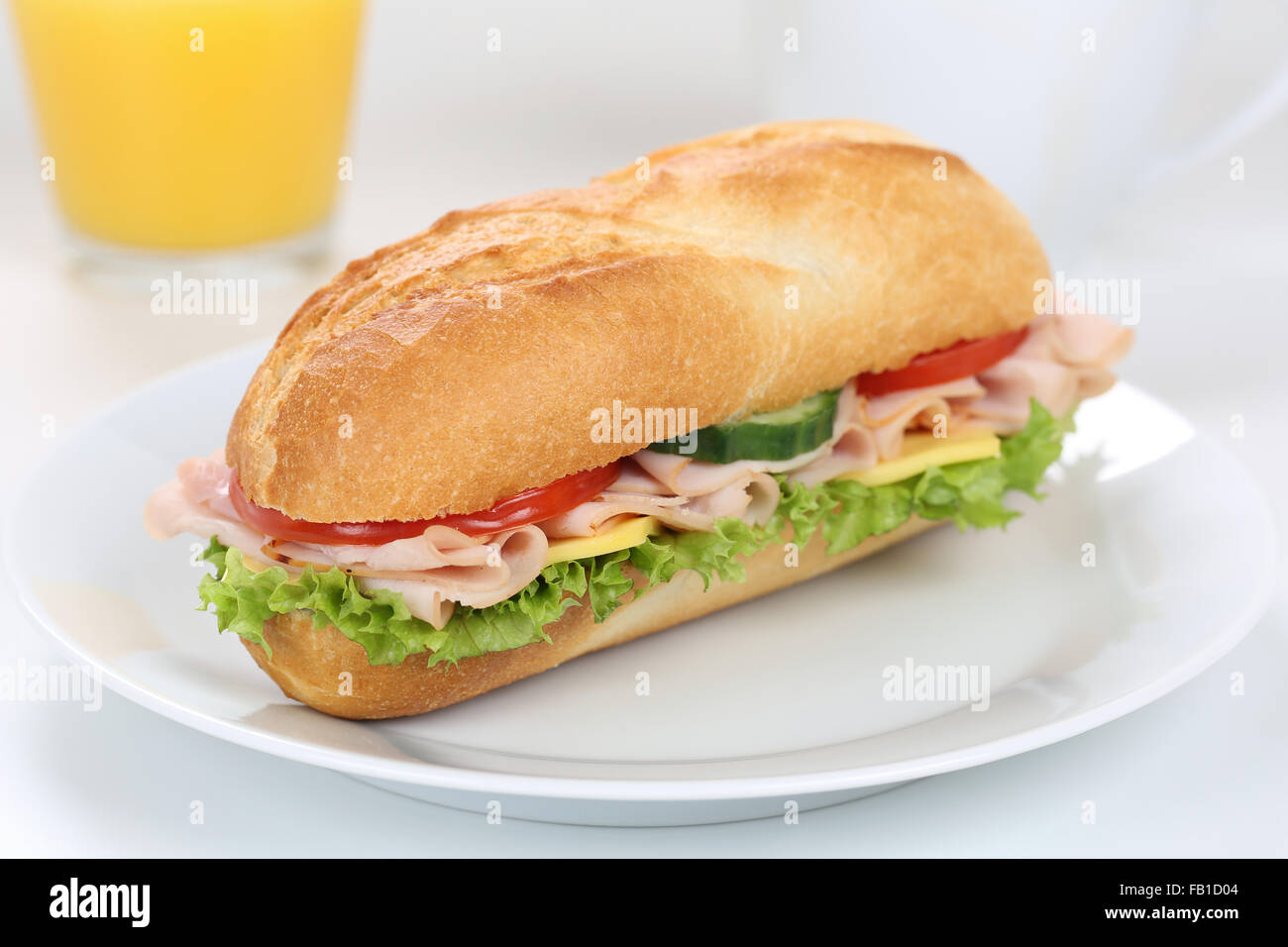 Sub deli sandwich baguette per colazione con prosciutto e formaggio, pomodori, lattuga e succo di arancia Foto Stock