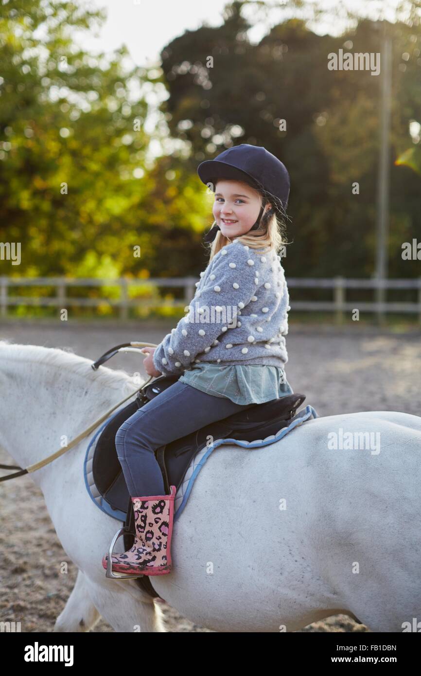 Ritratto di felice ragazza di equitazione pony bianco in arena equestre Foto Stock