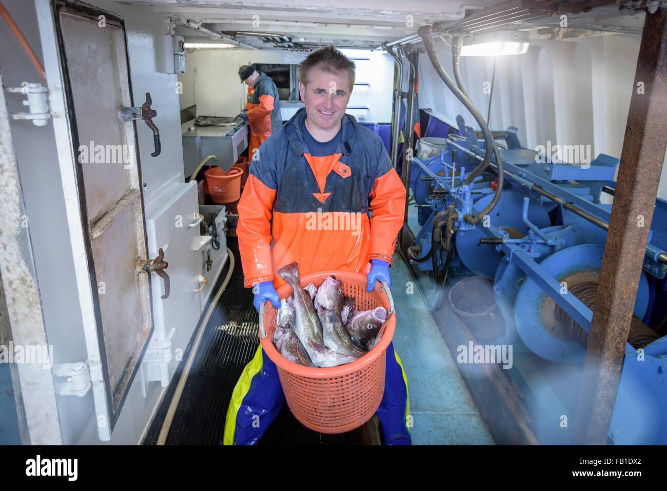 Pescatore con cesto di pesce sul peschereccio per traino, ritratto Foto Stock