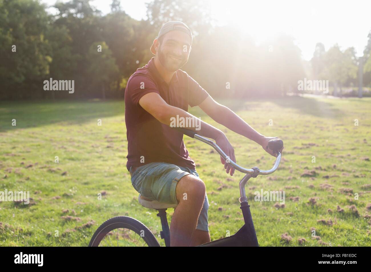 Ritratto di giovane uomo in bicicletta nel parco soleggiato Foto Stock