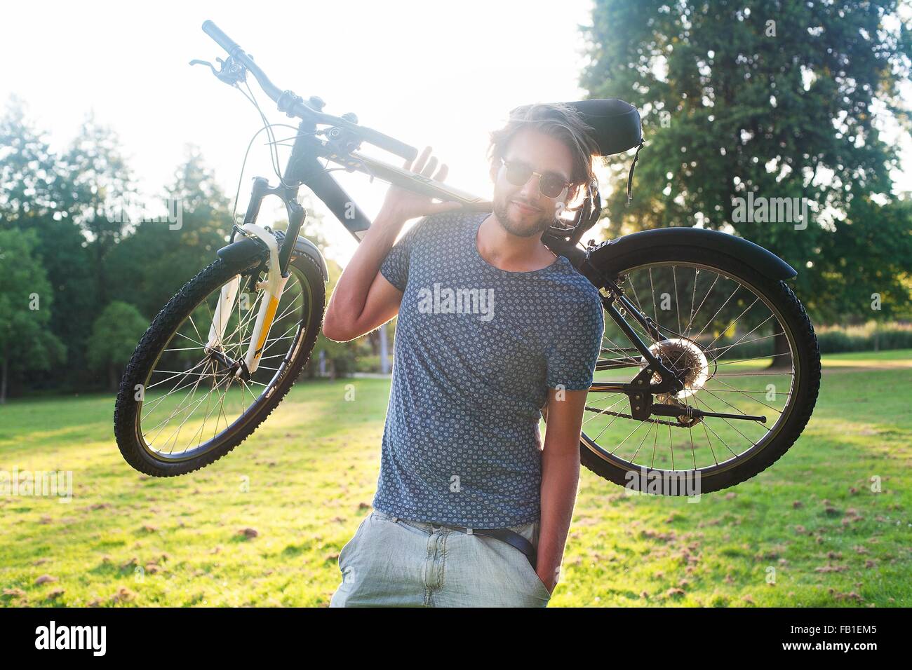 Ritratto di giovane uomo che porta la sua bicicletta nel parco al tramonto Foto Stock