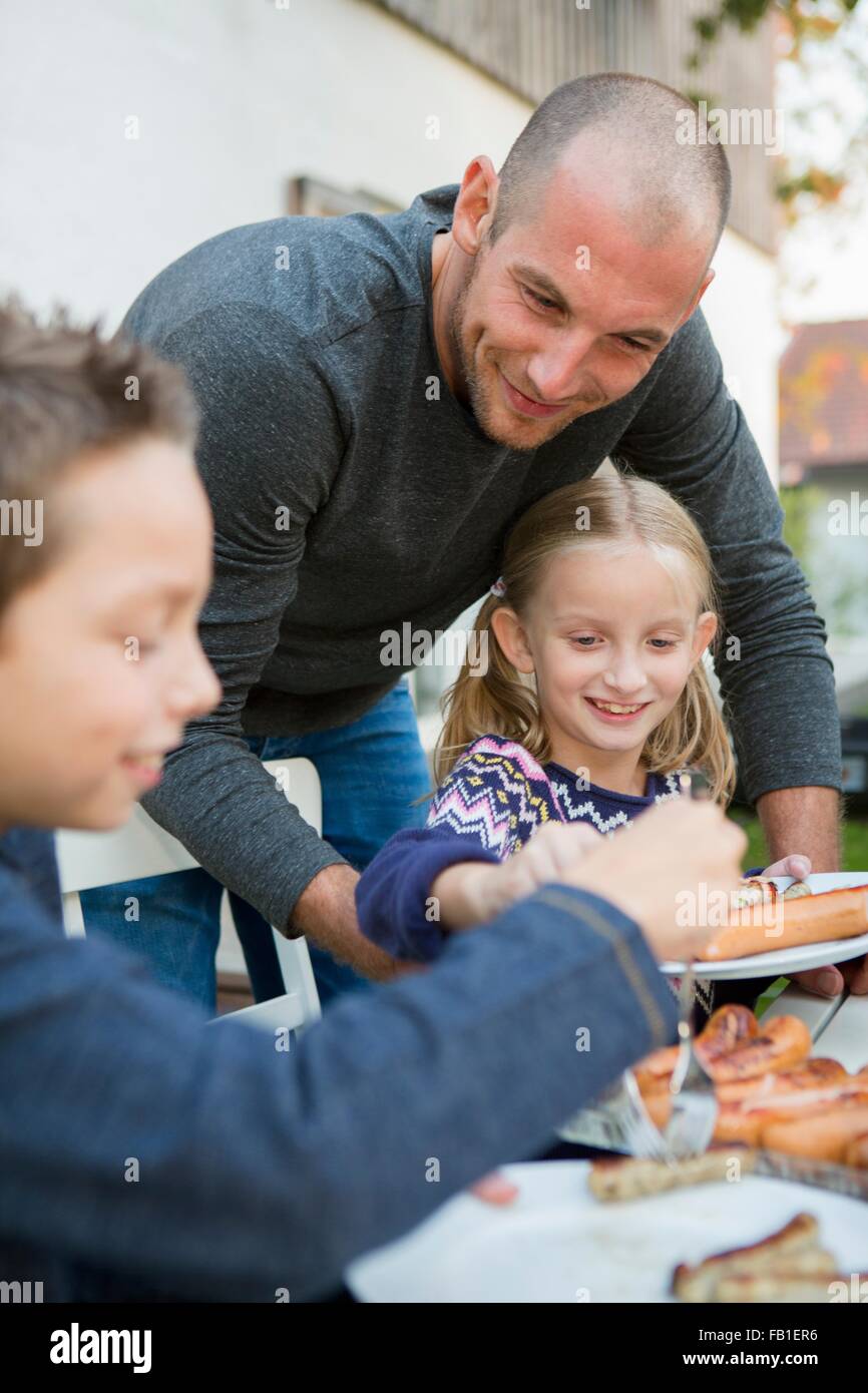 Padre aiutando i bambini in giardino barbecue tabella Foto Stock