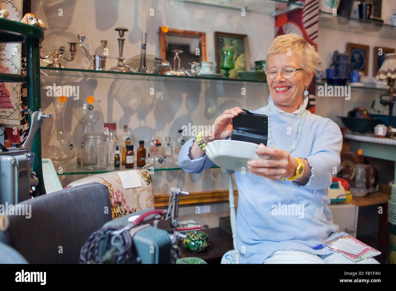 Donna matura fotografare la ciotola con lo smartphone nel negozio vintage Foto Stock