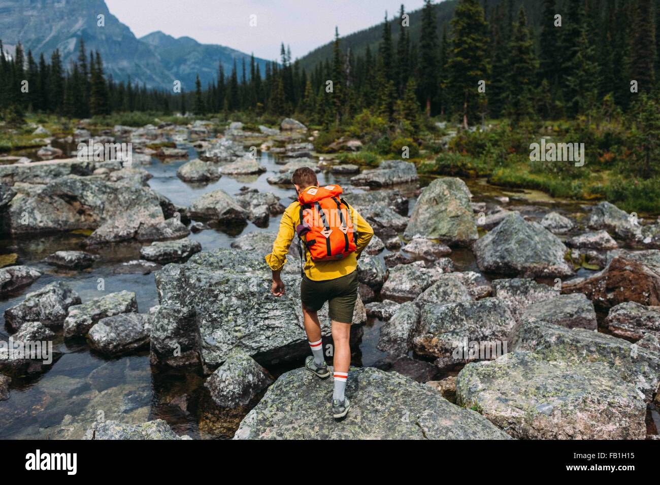 Vista posteriore della metà uomo adulto che porta uno zaino camminando sul alveo fluviale roccioso, Moraine Lake, il Parco Nazionale di Banff, Alberta Canada Foto Stock