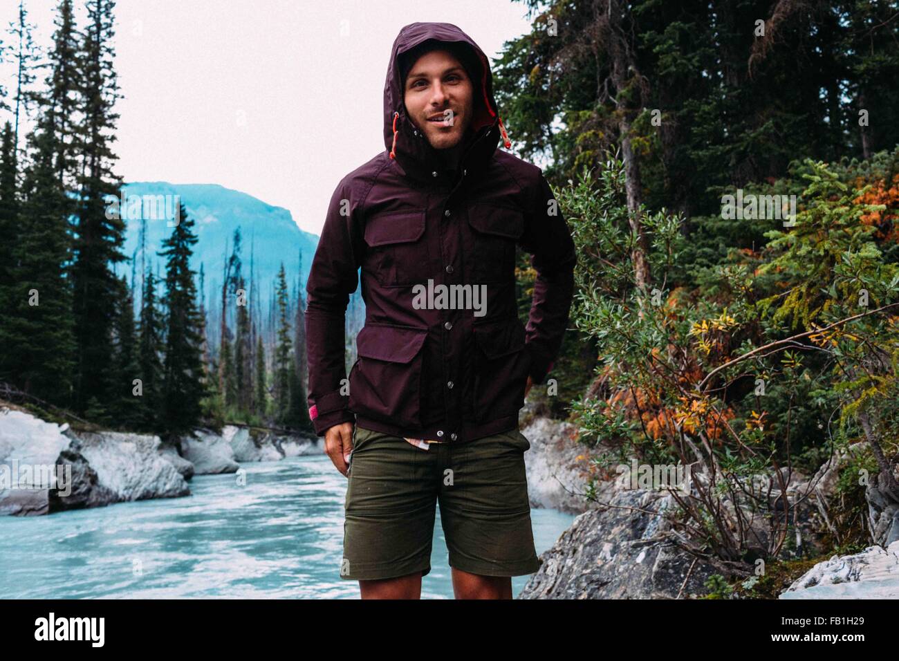 Metà uomo adulto fiume indossa cappuccio impermeabile fotocamera a sorridere al Lago Moraine il Parco Nazionale di Banff Alberta Canada Foto Stock