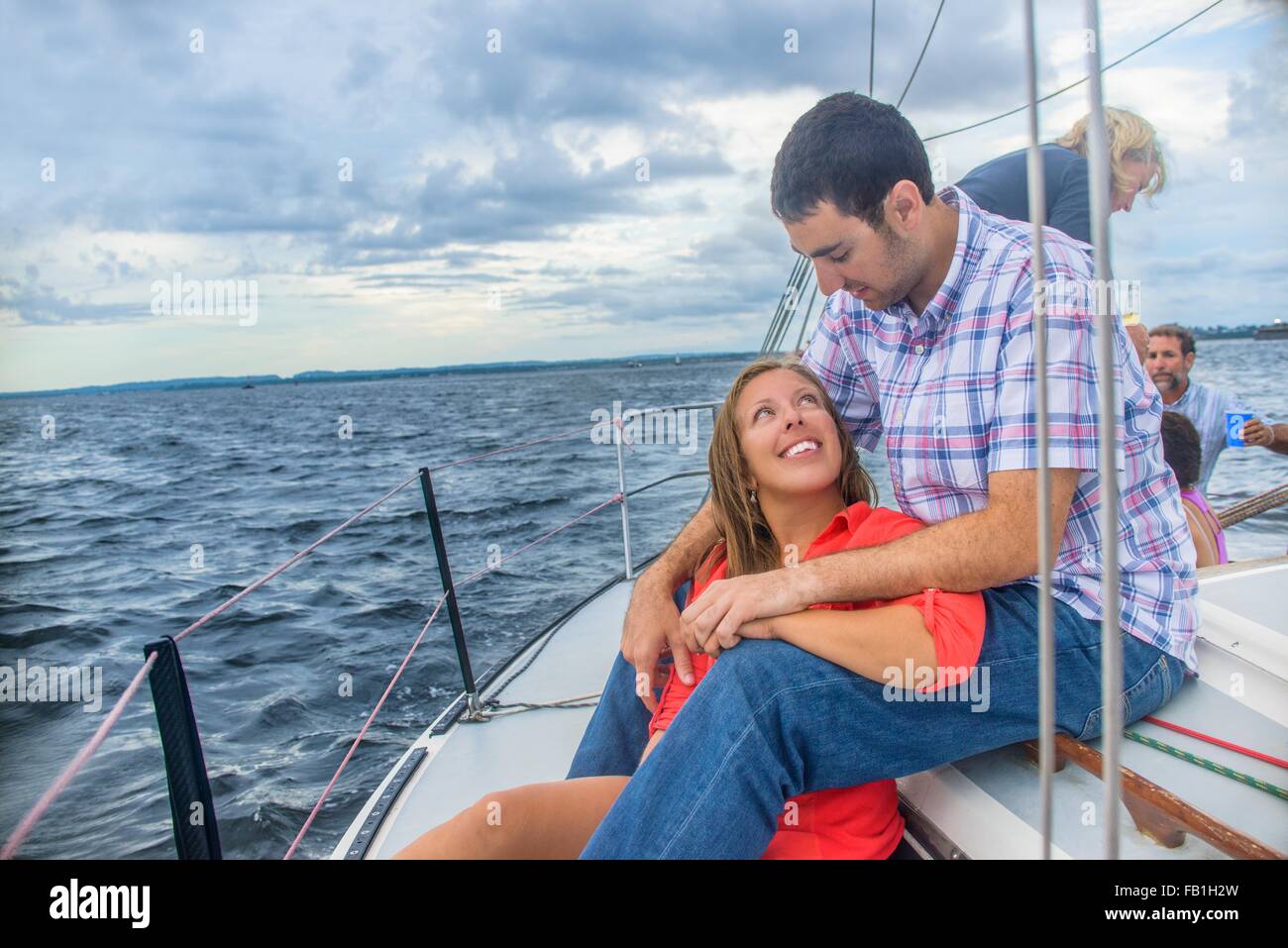 Giovane donna seduta tra giovani mans gambe su barche a vela, faccia a faccia sorridente Foto Stock