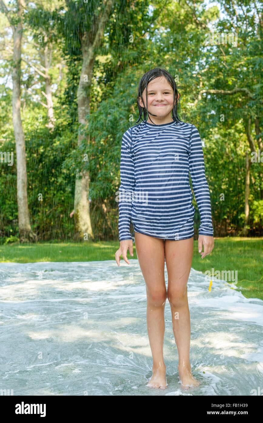 Ritratto di giovane ragazza in piedi su slip n slide acqua mat in giardino Foto Stock