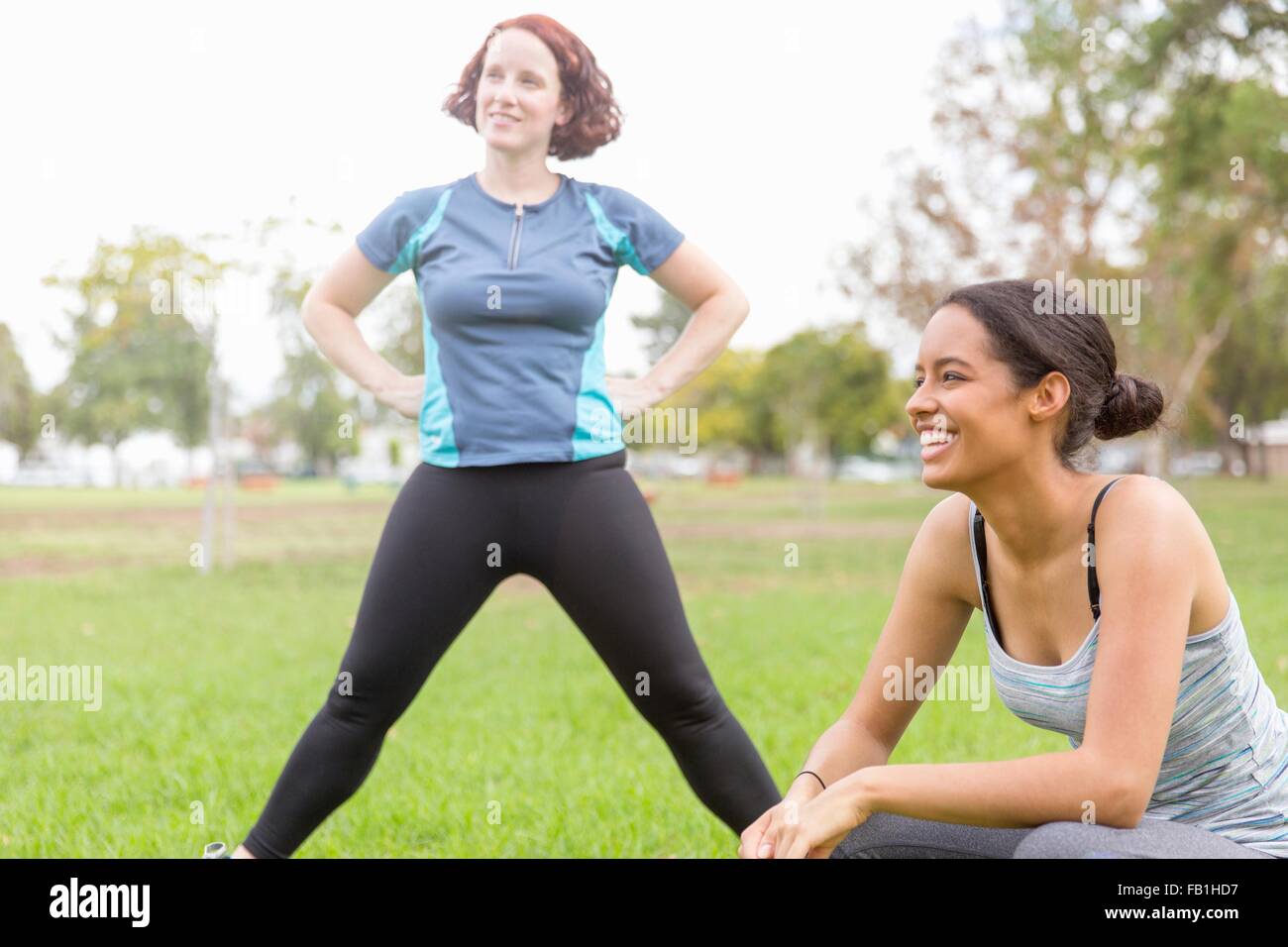 Le giovani donne di indossare abbigliamento sportivo nel campo stretching, guardando lontano sorridente Foto Stock