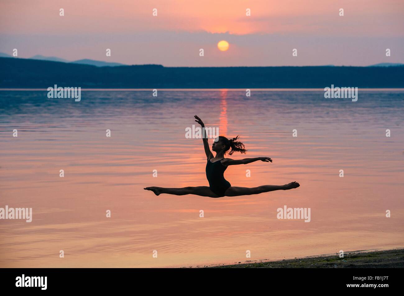 Vista laterale della ragazza dall' oceano al tramonto saltando a metà in aria, braccia alzate facendo i gruppi Foto Stock
