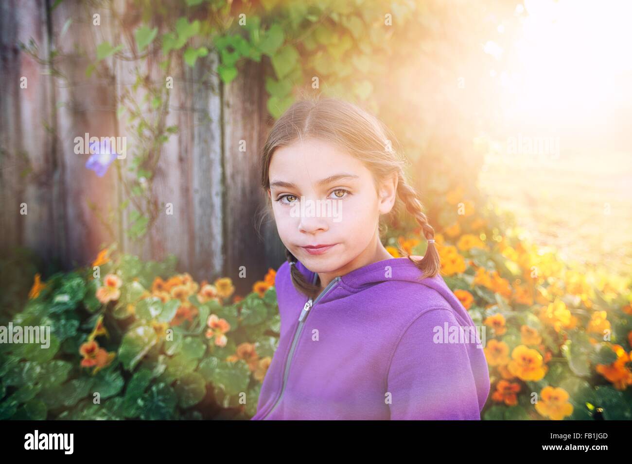 Ritratto di ragazza con trecce nella parte anteriore di fiori d'arancio guardando la fotocamera Foto Stock Ritratto di ragazza con trecce nella parte anteriore di fiori d'arancio guardando la fotocamera Foto Stock