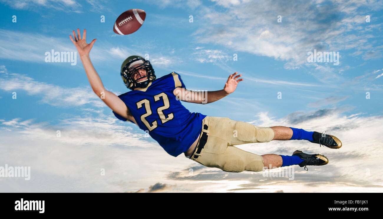 Un adolescente di sesso maschile giocatore di football americano raggiungendo per la cattura di sfera metà aria contro il cielo blu Foto Stock