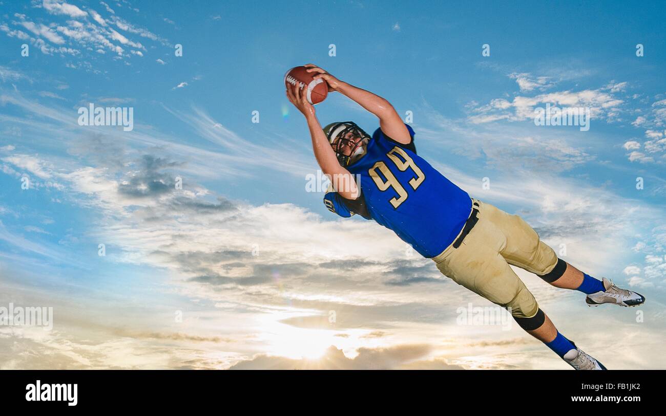 Un adolescente di sesso maschile giocatore di football americano la cattura di sfera metà aria contro il cielo blu Foto Stock