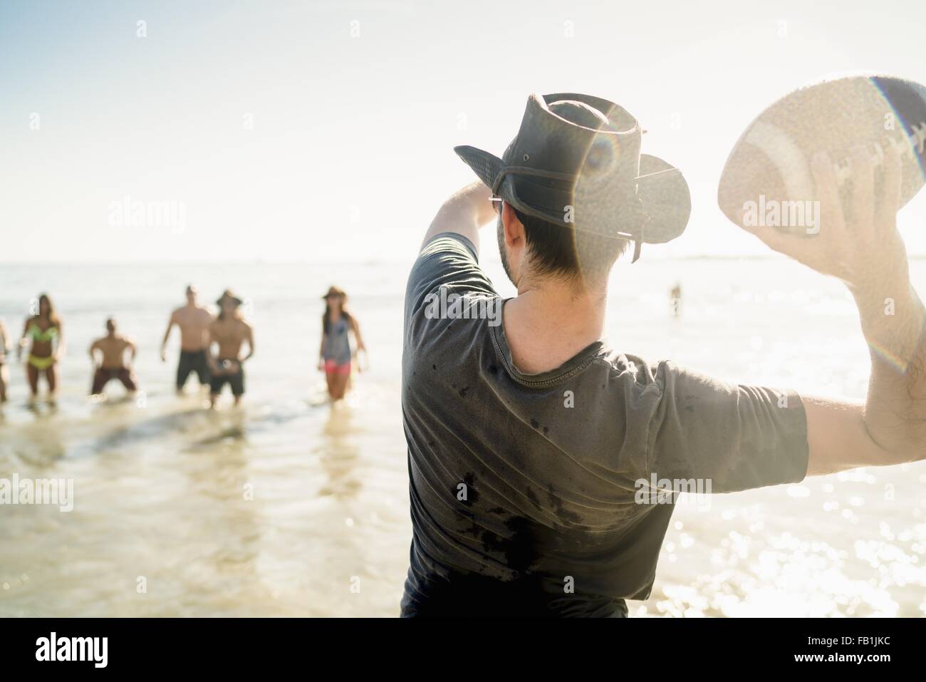 Giovane uomo gettando il football americano la sfera di amici in mare a Newport Beach, California, Stati Uniti d'America Foto Stock