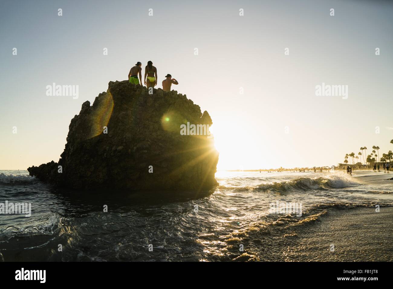 Silhouette di amici adulti sulla formazione di roccia al tramonto, Newport Beach, California, Stati Uniti d'America Foto Stock