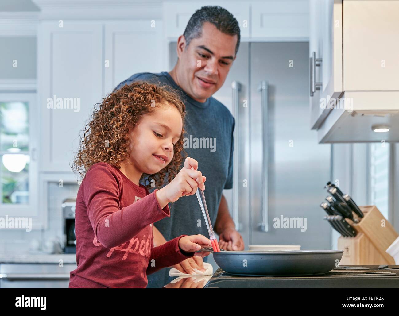 Padre aiutando la figlia cuocere sul piano di cottura in cucina Foto Stock