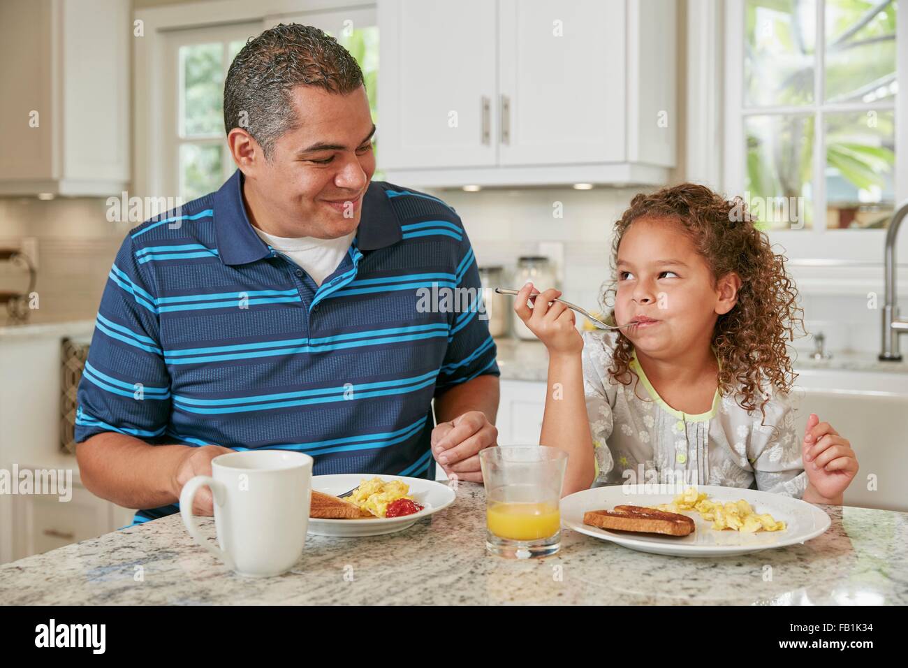 Padre e figlia fianco a fianco al bancone cucina mangiare la prima colazione sorridente Foto Stock