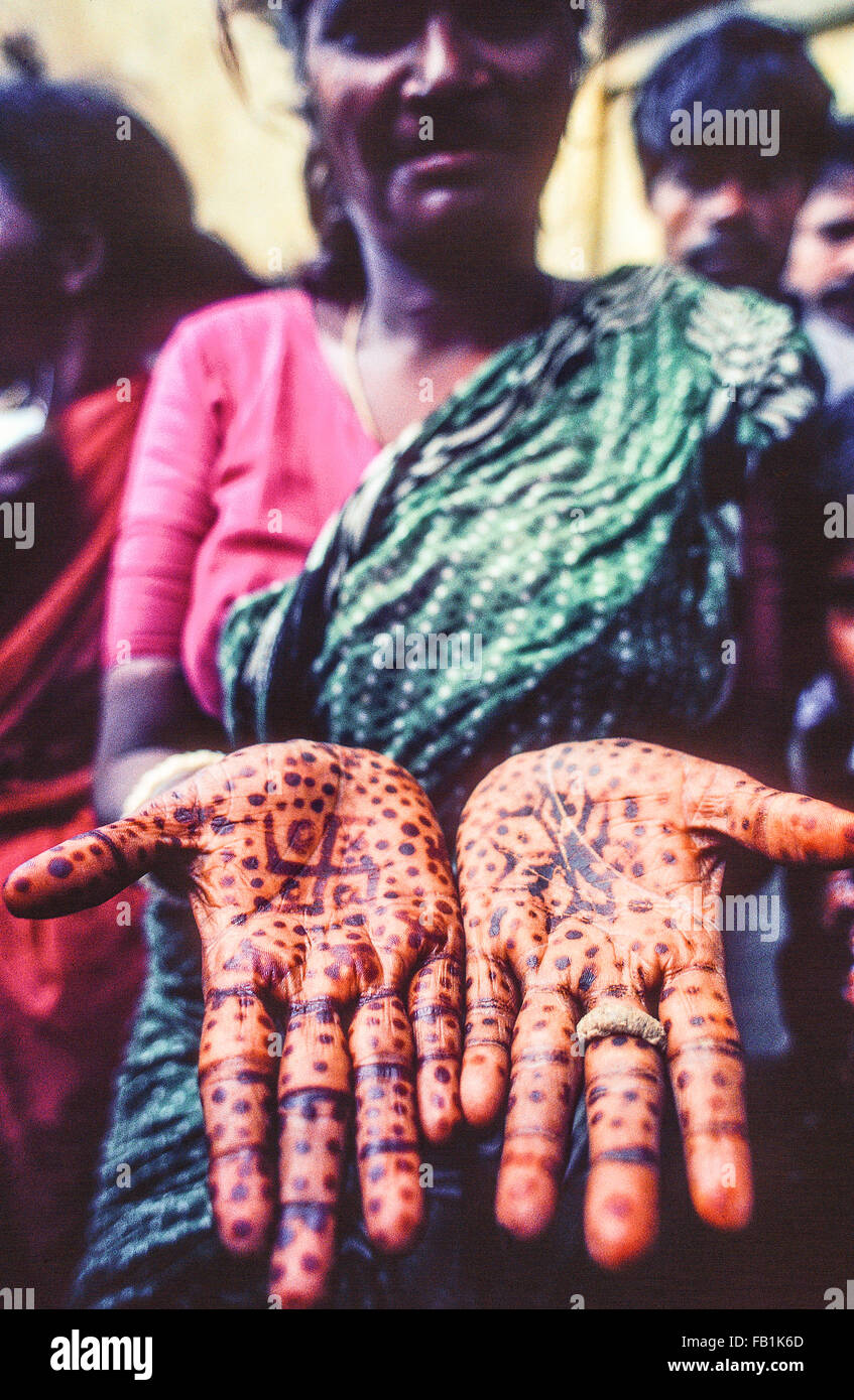 Una donna Indiana che contiene la sua henna tinto mani, palme, con puntini colorati e una croce uncinata. Foto Stock