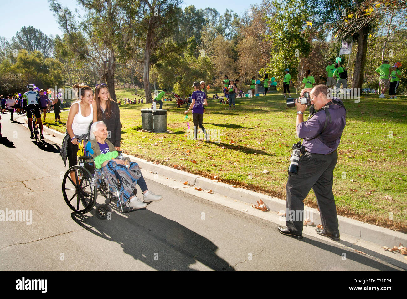 Una sedia a rotelle partecipante in una raccolta fondi di beneficenza a piedi per le vittime dell'Alzheimer attraversa la linea del traguardo e comporta per il fotografo ufficiale in una Laguna Niguel, CA, parco. Nota nipote spingendo sedia a rotelle. Foto Stock