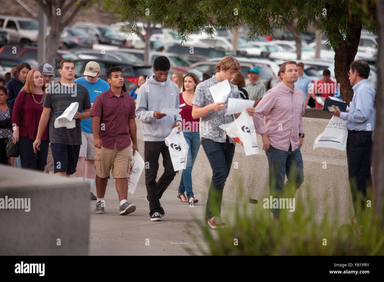 Portando i sacchetti di plastica per la letteratura, multirazziale di alta scuola gli studenti e i genitori che arrivano a un college fair di Aliso Viejo, CA. Nota piena parcheggio in background. Foto Stock