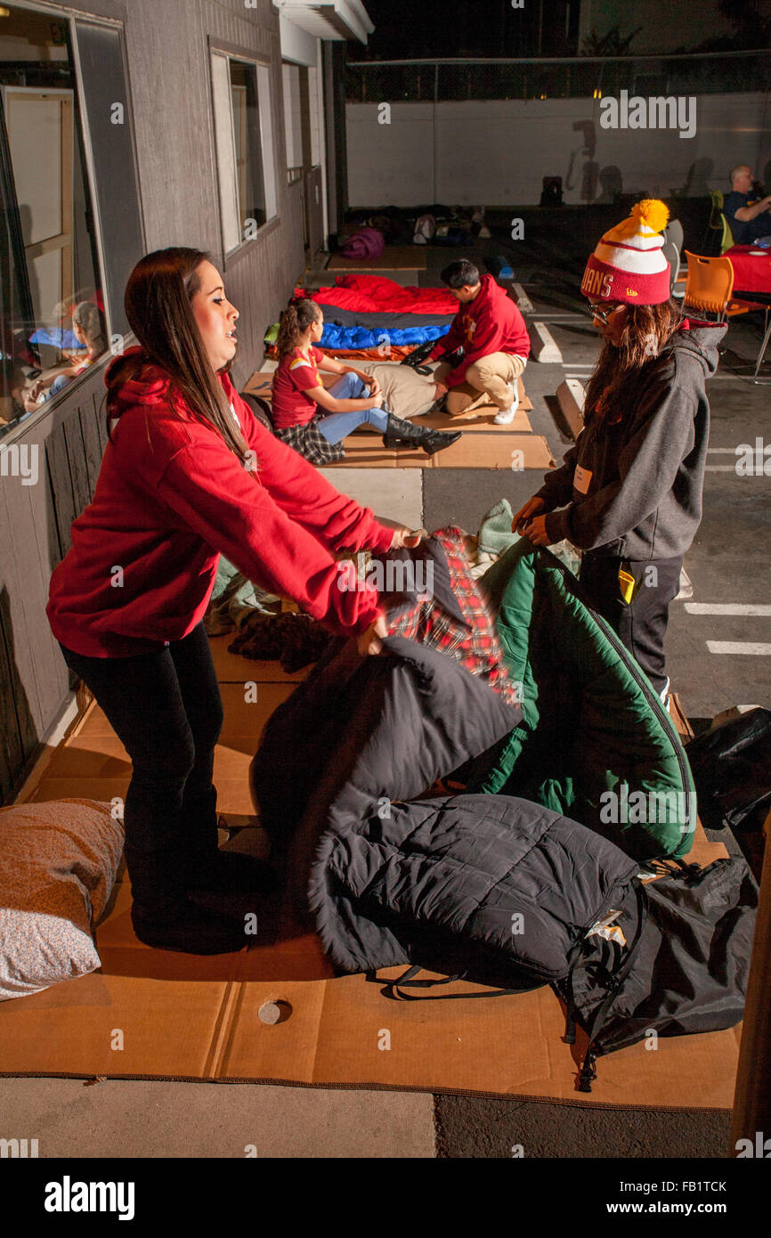 Che desiderano identificare con il dramma dei senzatetto, due giovani donne srotolare i sacchi a pelo su un foglio di cartoncino a dormire all'aperto nel parcheggio di un rifugio in Costa Mesa, CA. Foto Stock