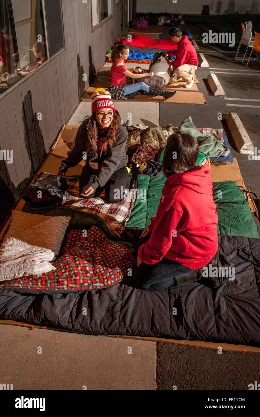 Che desiderano identificare con il dramma dei senzatetto, due giovani donne srotolare i sacchi a pelo su un foglio di cartoncino a dormire all'aperto nel parcheggio di un rifugio in Costa Mesa, CA. Foto Stock